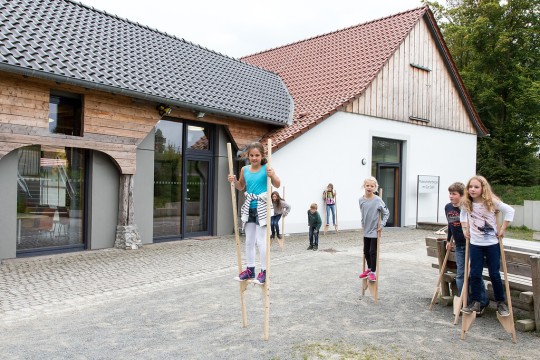 Kinder spielen vor der Museumsherberge mit Stelzen.